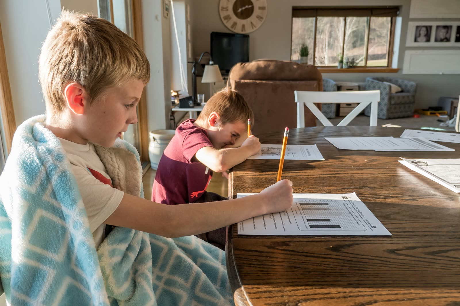 Two boys doing homework worksheets at a dining table in natural light